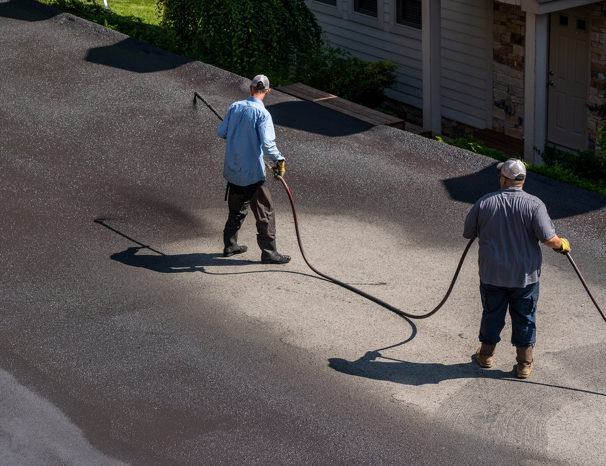 Workers applying blacktop sealer to asphalt street using a spray to provide a protective coat against the elements